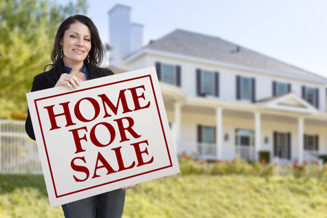 Smiling Hispanic Female Holding Sold For Sale Sign In Front of Beautiful House.
